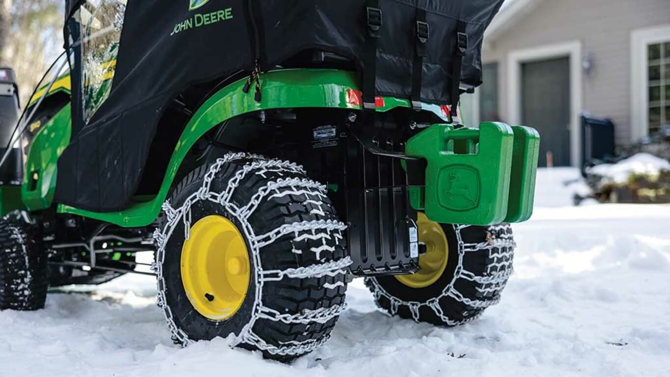 Close-up of snow chains around the back tires of a green riding mower.