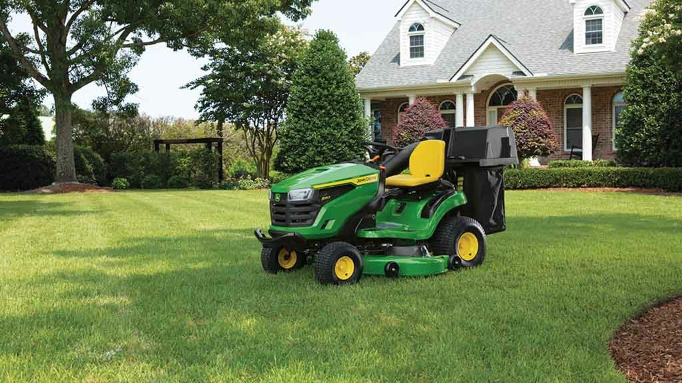 A green riding mower sitting on a well-kept lawn with a bagging attachment.