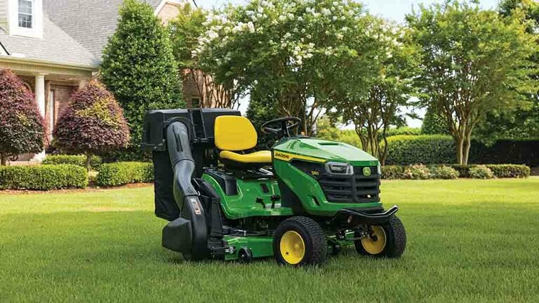 A green riding mower with a bagging attachment sitting on a lawn with short even grass.