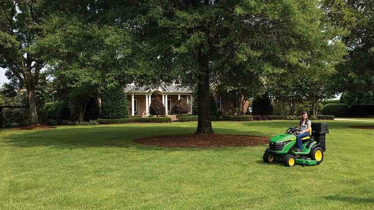 A wide view of a well-kept lawn, off to the side a green riding mower with a bagging attachment.