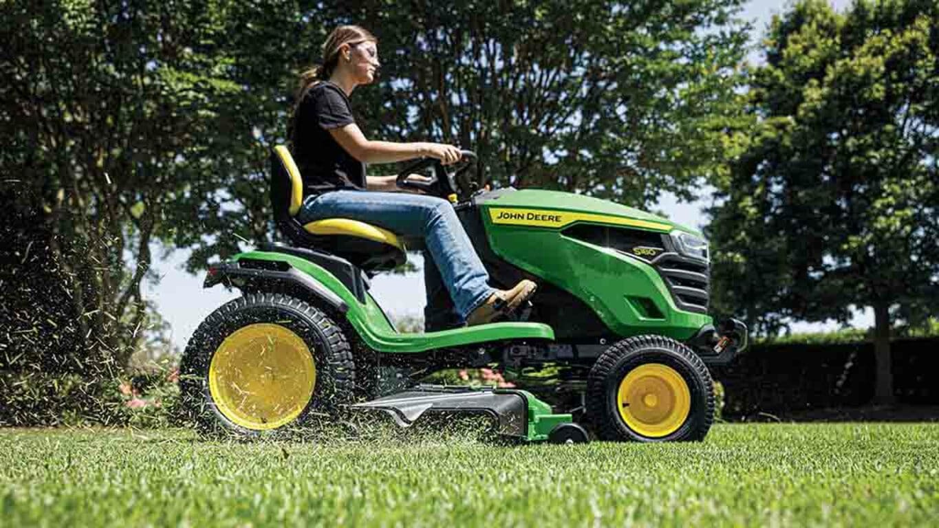 Close-up of grass being blown out the side of a green deck attached to a green riding mower.