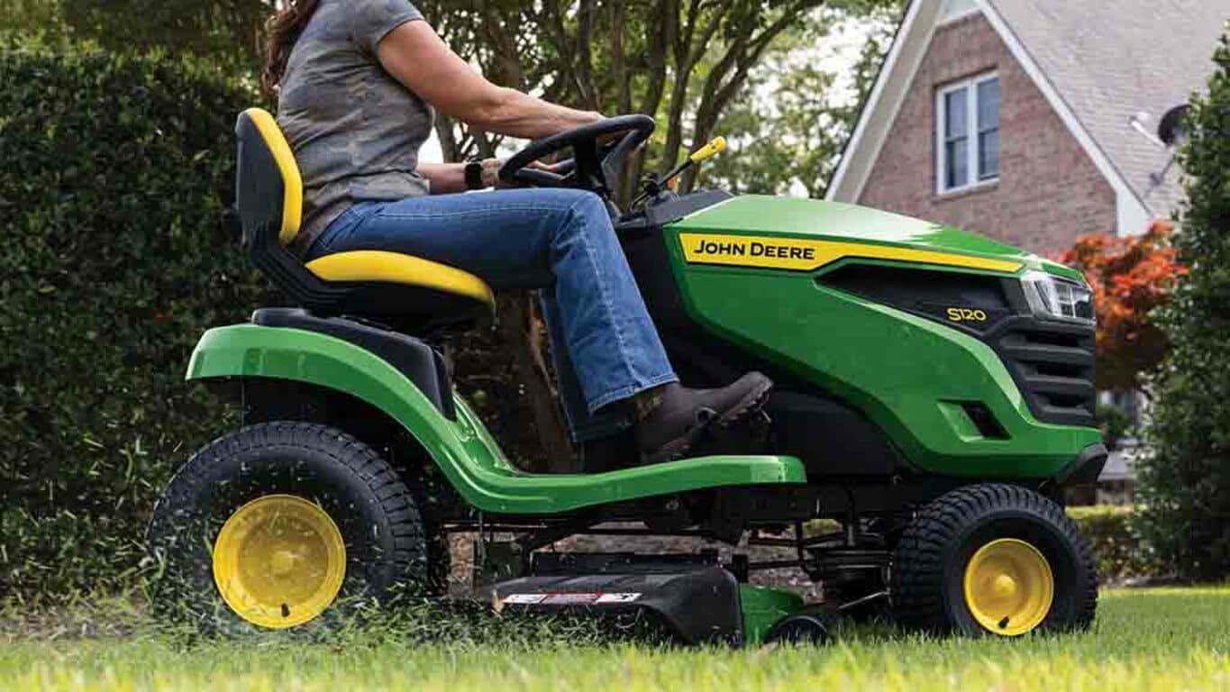 A close-up right side view of a green riding mower with grass clippings coming out the side of the deck.
