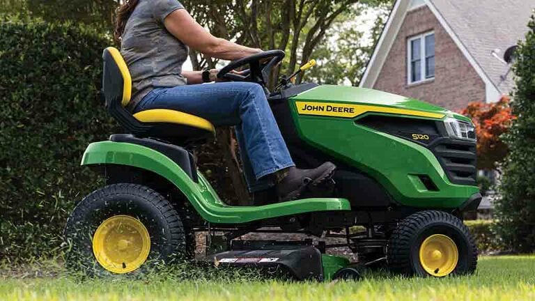 A close-up right side view of a green riding mower with grass clippings coming out the side of the deck.