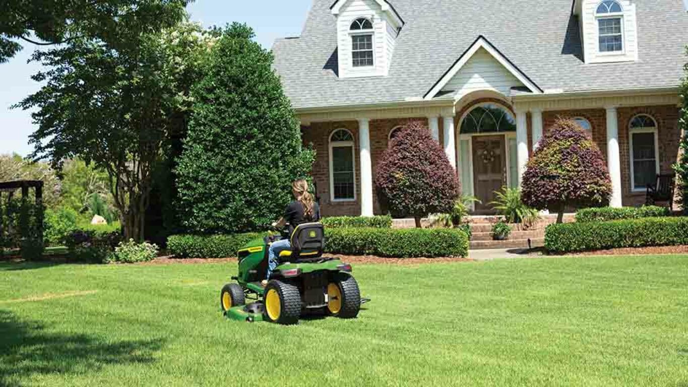 A person driving back-and-forth on a grassy lawn with a green riding mower.