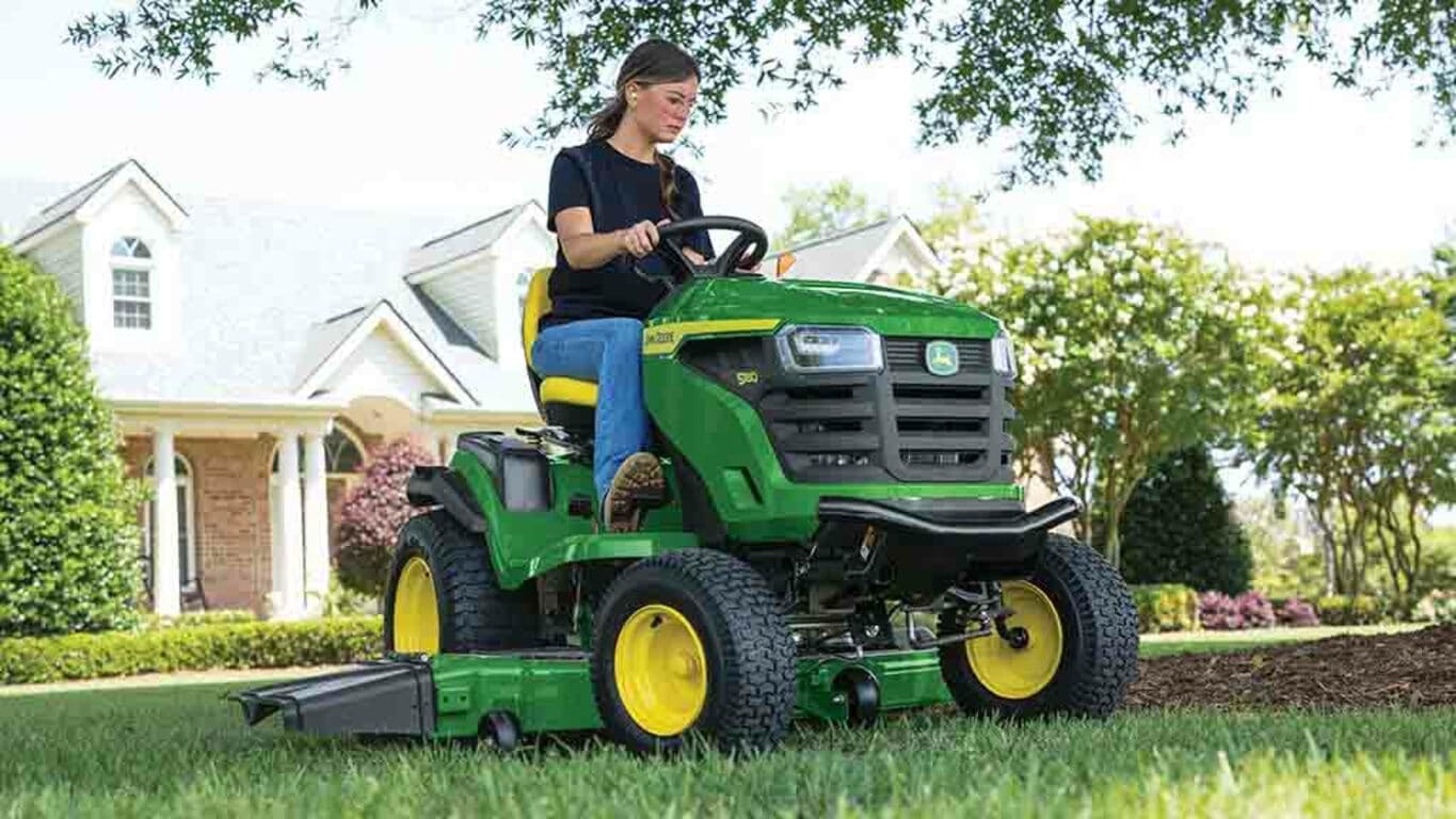 A person rounding the edge of a patch of mulch with a green riding mower.