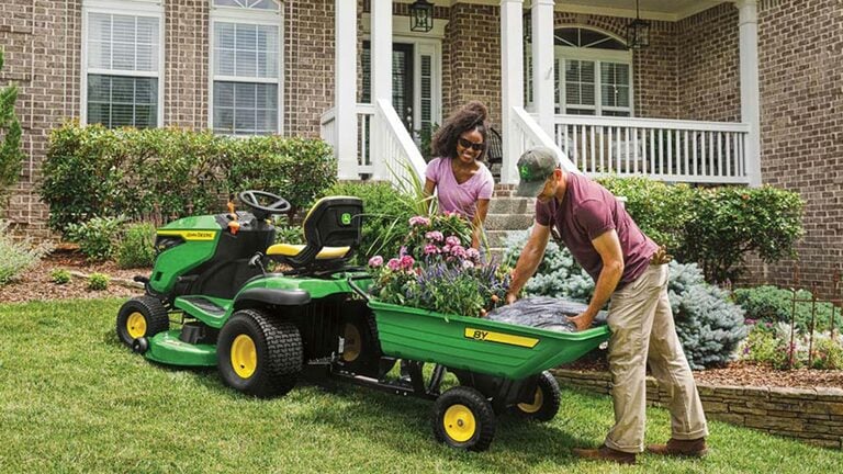 Deux personnes se servent d’un tracteur de pelouse S130 et d’une remorque arrière pour planter des fleurs