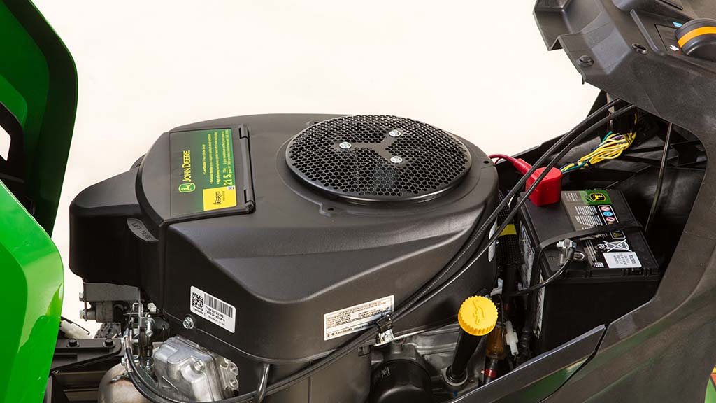 Gros plan d’un moteur bicylindre en V sous le capot vert d’une tondeuse.