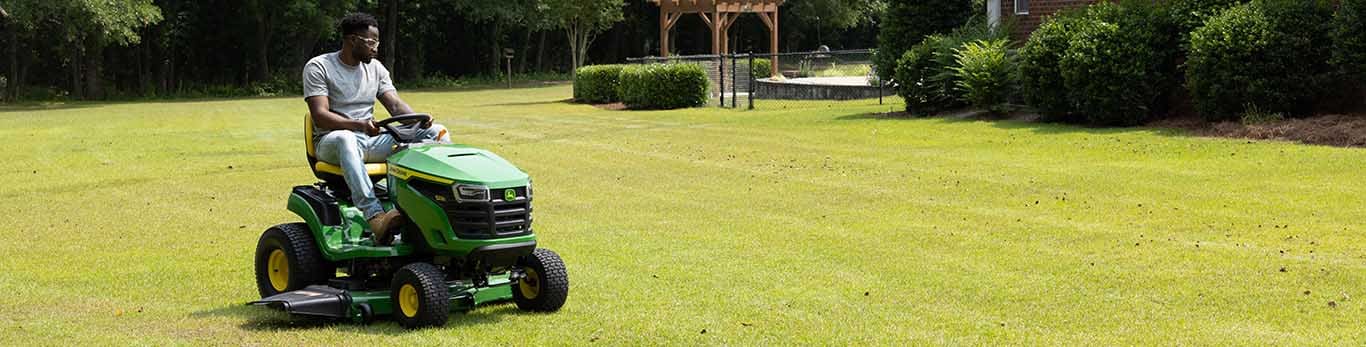 Une personne conduisant une tondeuse autoportée verte sur une grande pelouse d'herbe courte et uniforme.