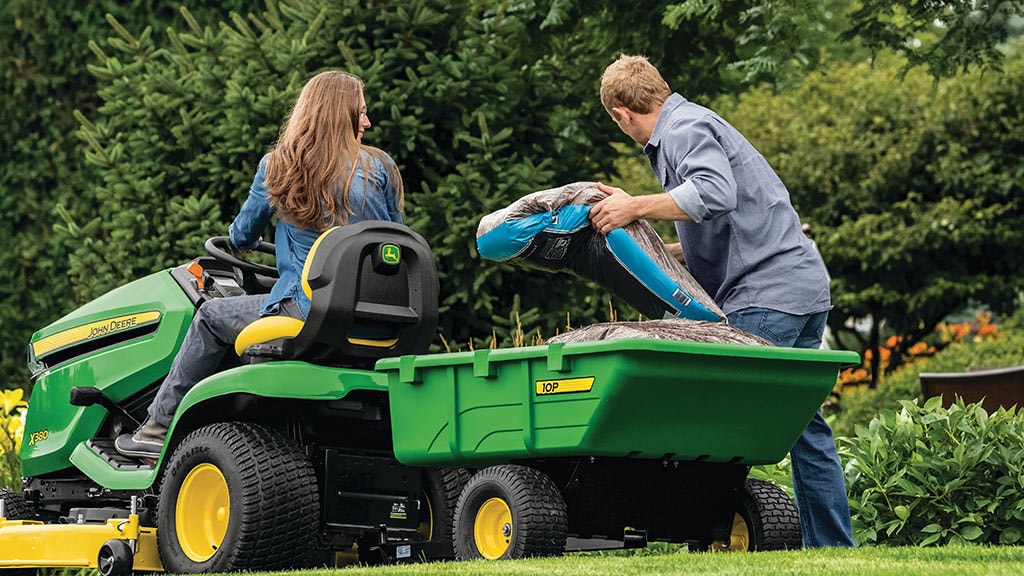 woman on a X300 lawn mower with man unloading top soil bags from cart