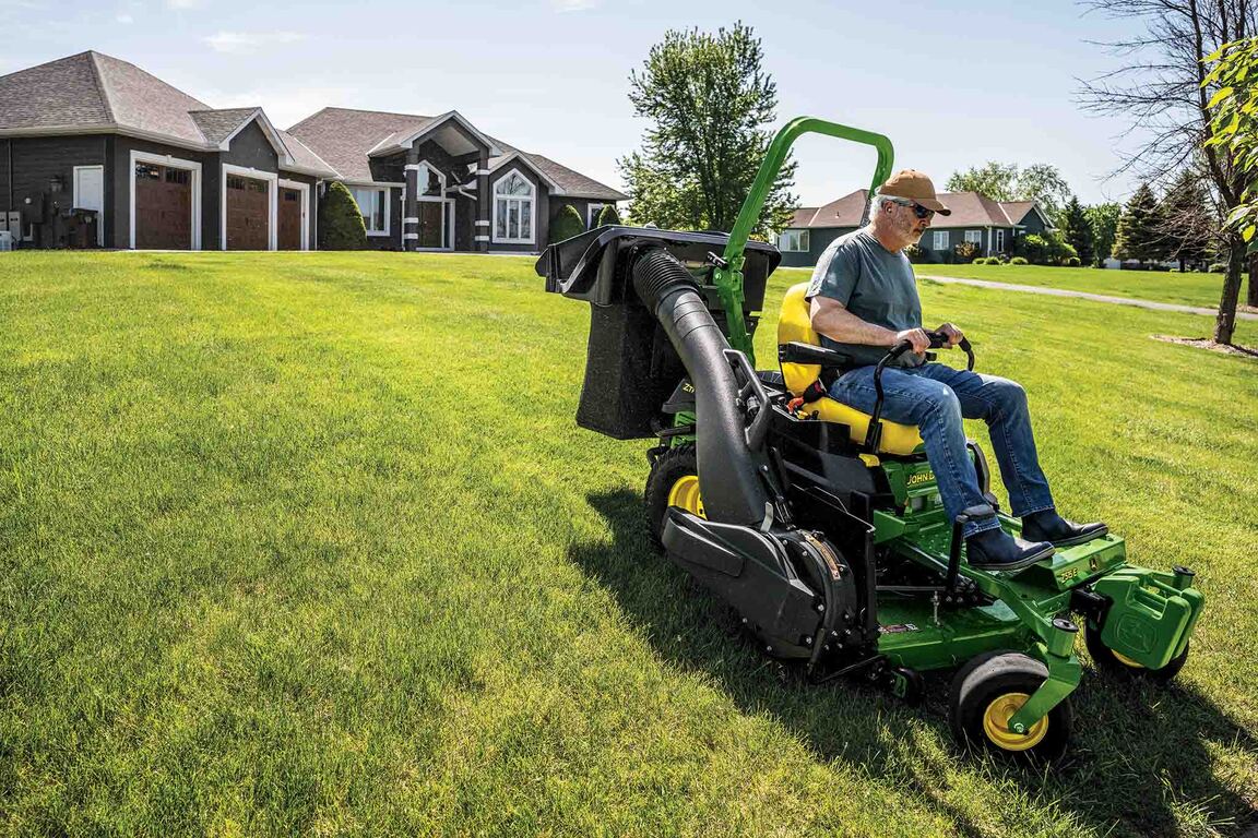 A Z515E zero-turn mower with a bagging attachment mows a wide-open lawn in front of a residence.