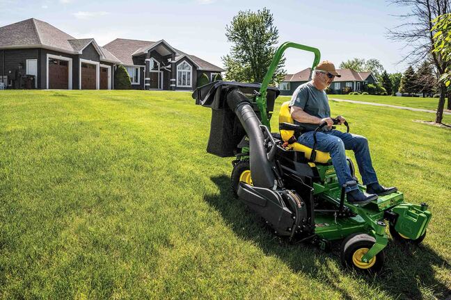 A Z515E zero-turn mower with a bagging attachment mows a wide-open lawn in front of a residence.