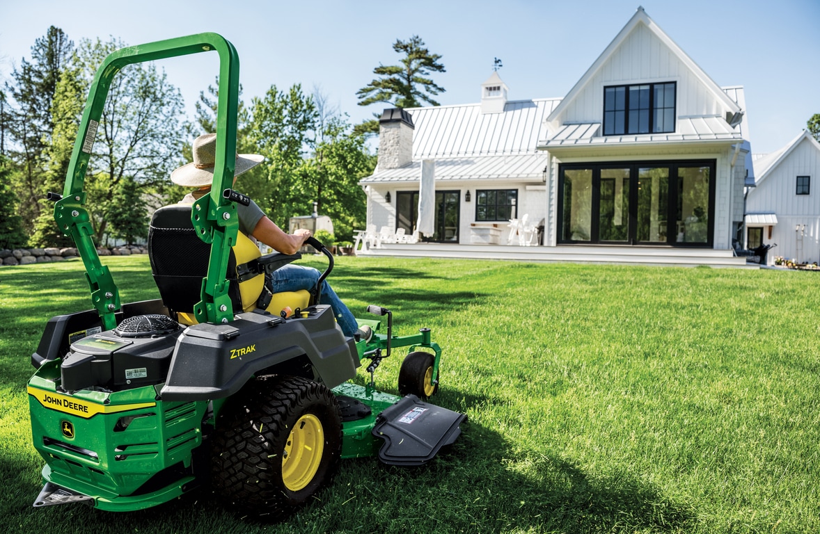 A rear-right-facing view of a green zero-turn mower and its engine as it mows the lawn of a residence.