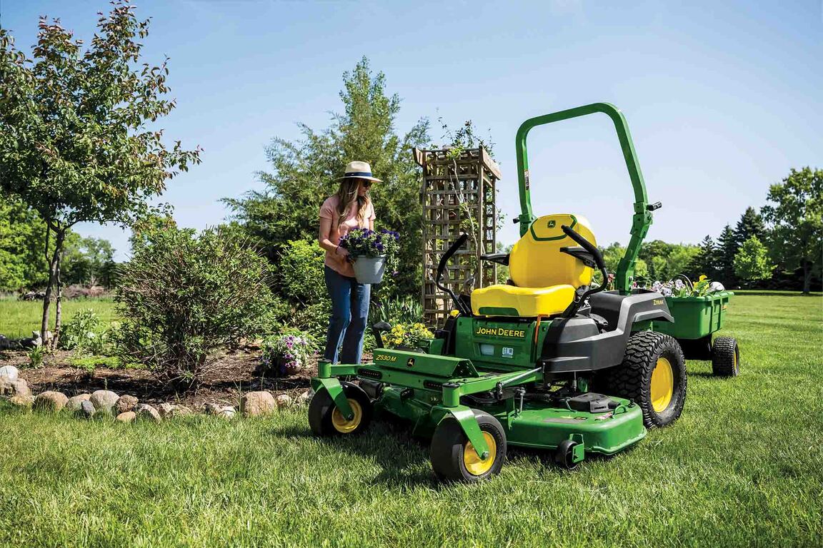 A person with a potted plant walks towards a poly cart attached to the back of a Z530M zero-turn mower.