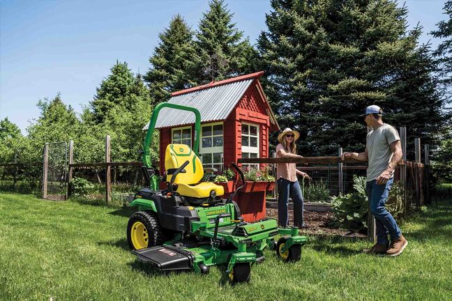 A Z560R zero-turn mower rests on a well-kept lawn next to two people chatting near fenced-in garden.