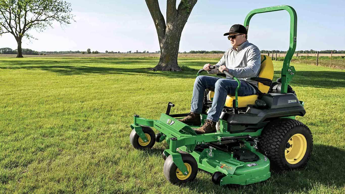 A green zero-turn mower being used to tend a large wide-open field.