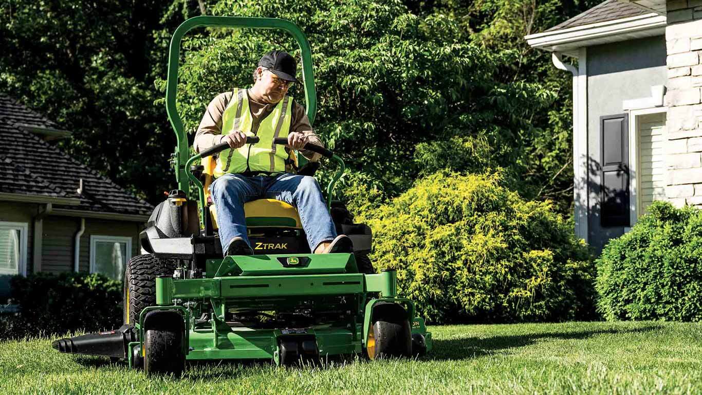 Grass being mowed in front of a residence by a landscaper on a green zero-turn mower.