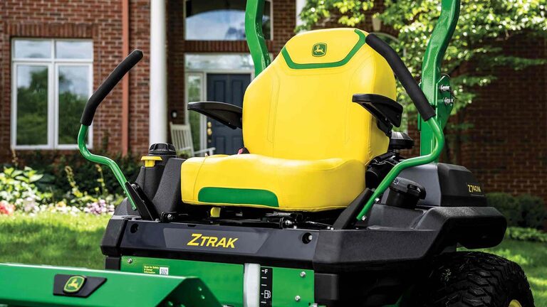 A zoomed-in shot of a yellow zero-turn mower seat with green detailing in front of a residence.
