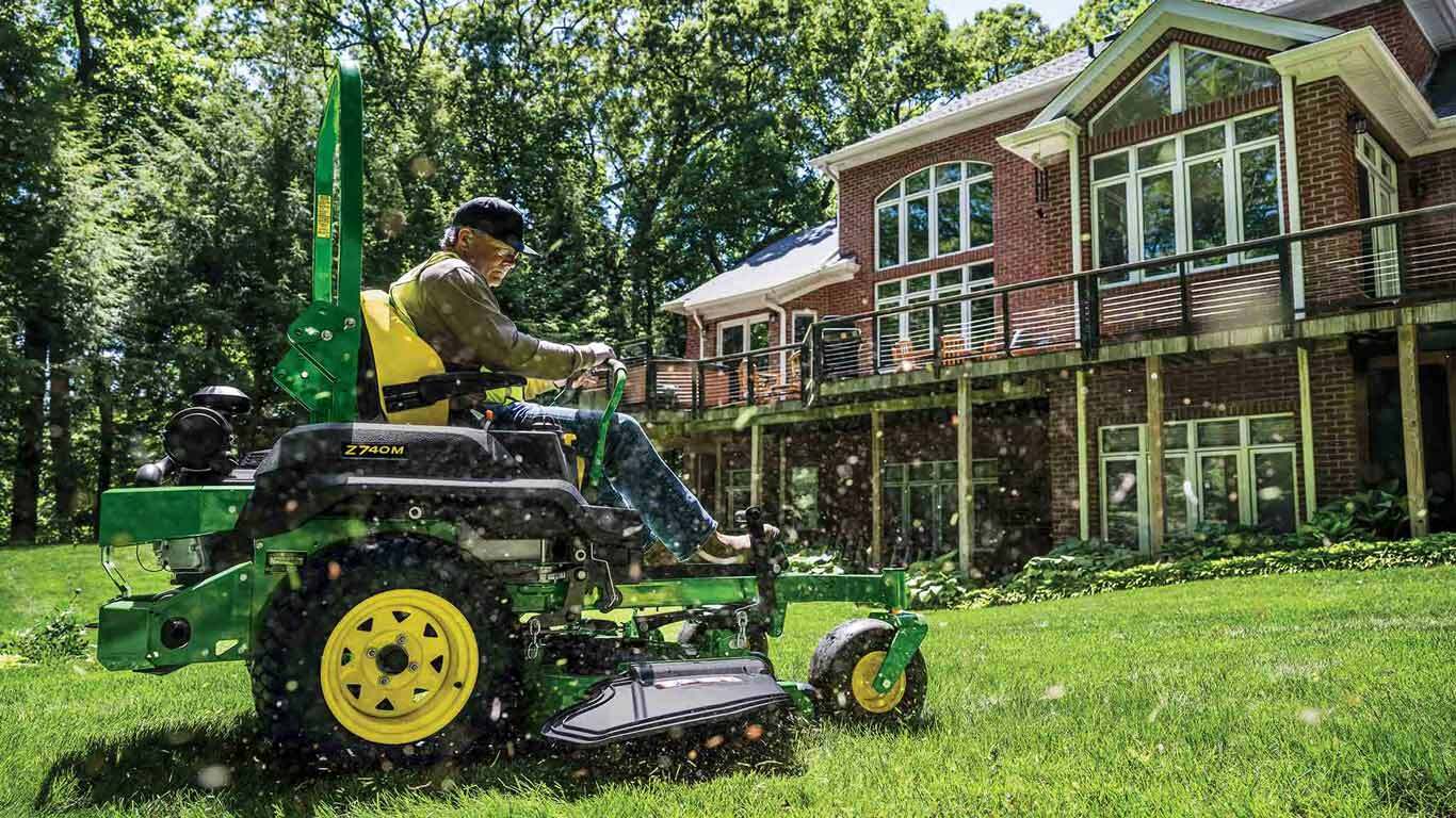 Grass being mowed behind a residence by a landscaper on a green zero-turn mower.