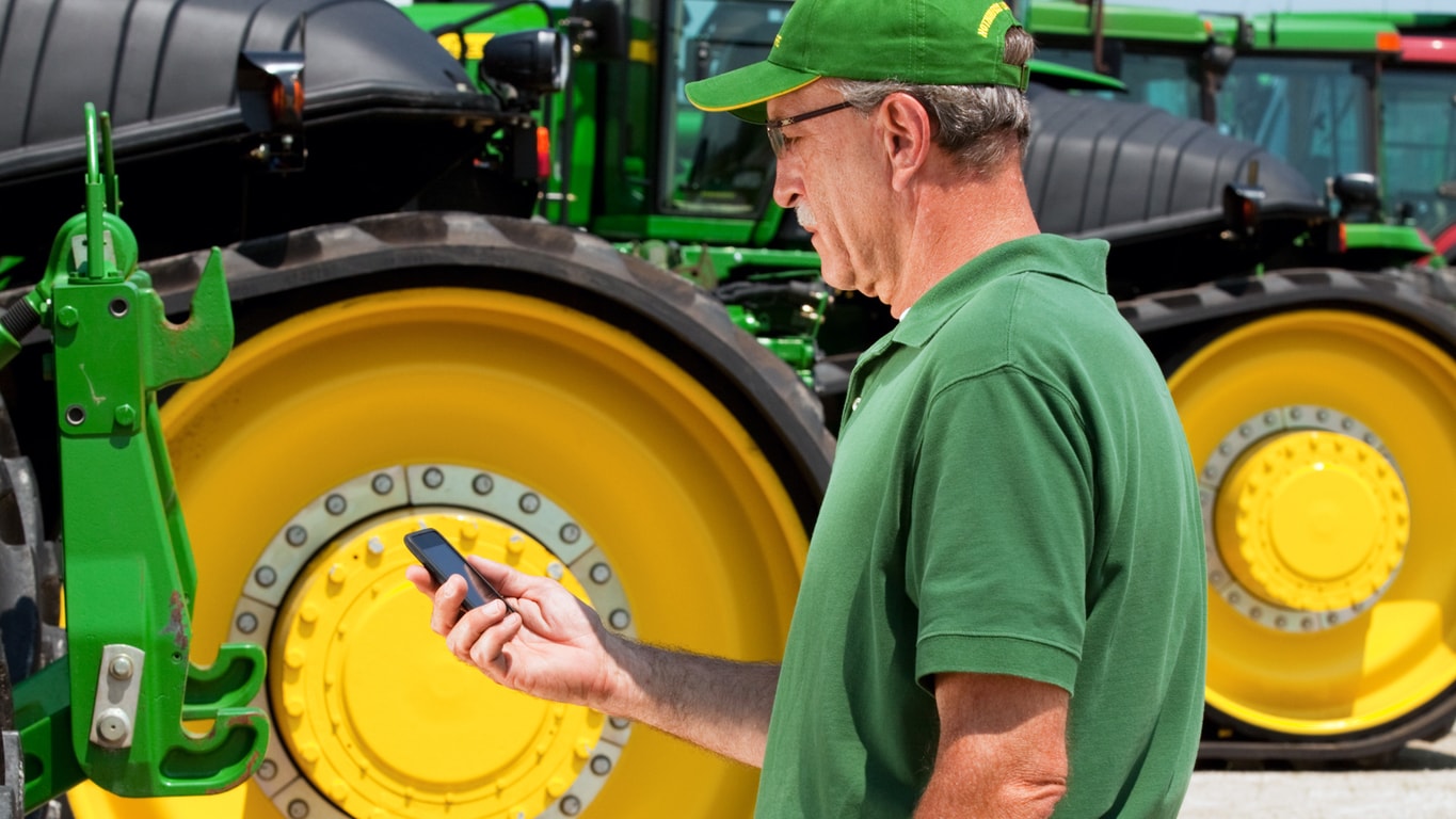 homme tenant un téléphone intelligent à côté d'un tracteur