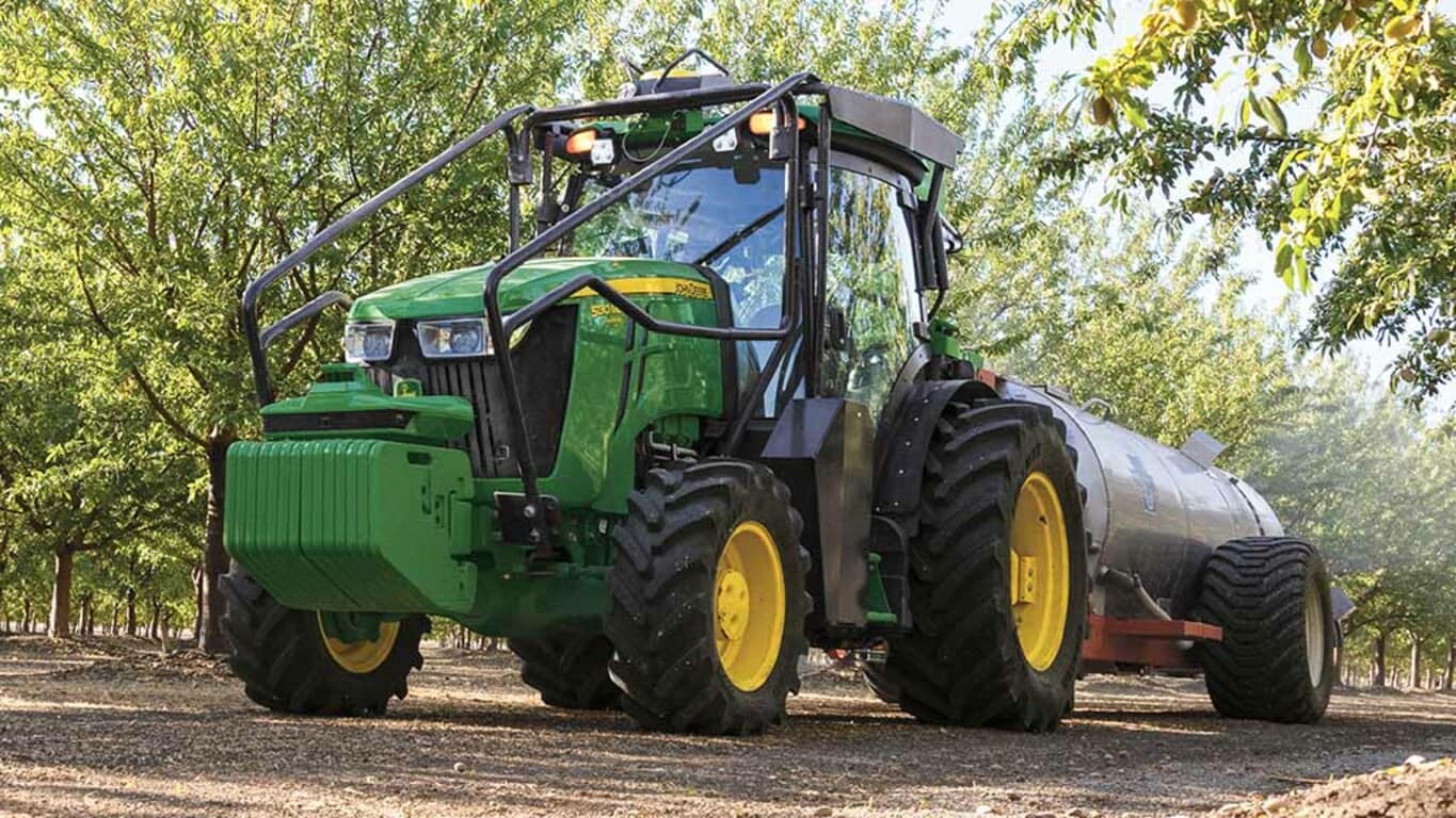 Tracteur 5EN conduit dans un verger de cerisiers en fleurs.