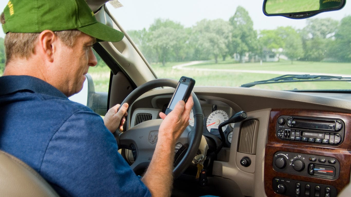 Un homme utilisant son téléphone portable assis dans son véhicule pour vérifier ses machines avec JDLink John Deere.