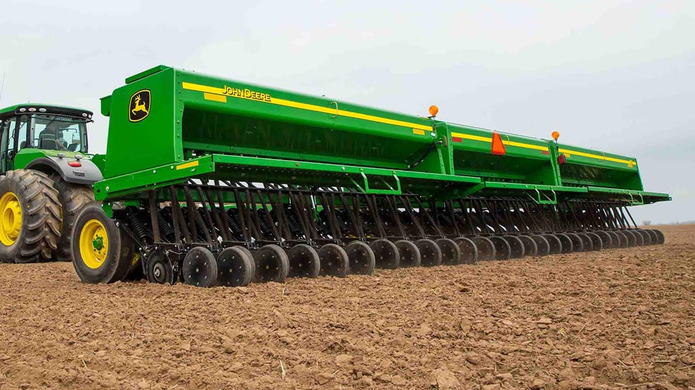 Vue latérale arrière d’un semoir à grain John Deere 455 de 35&nbsp;pieds repliable à l’avant, attelé à un tracteur John Deere dans un champ.