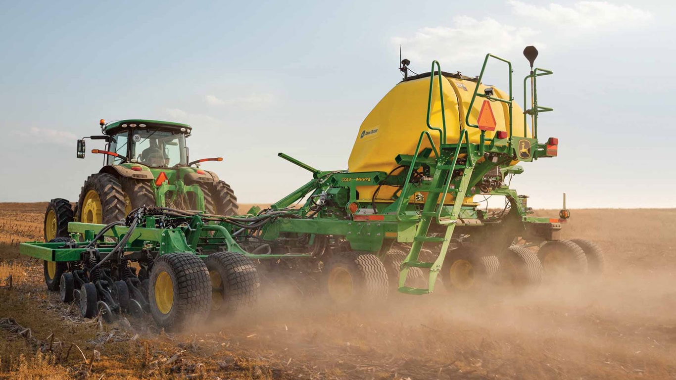 Vue latérale arrière d’un semoir pneumatique sans labour John Deere tracté dans un champ par un tracteur John Deere.