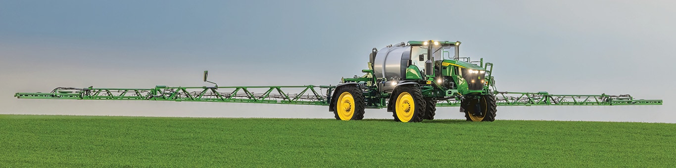 A John Deere Self-Propelled Sprayer &ndash; with booms fully extended &ndash; spraying in a field.