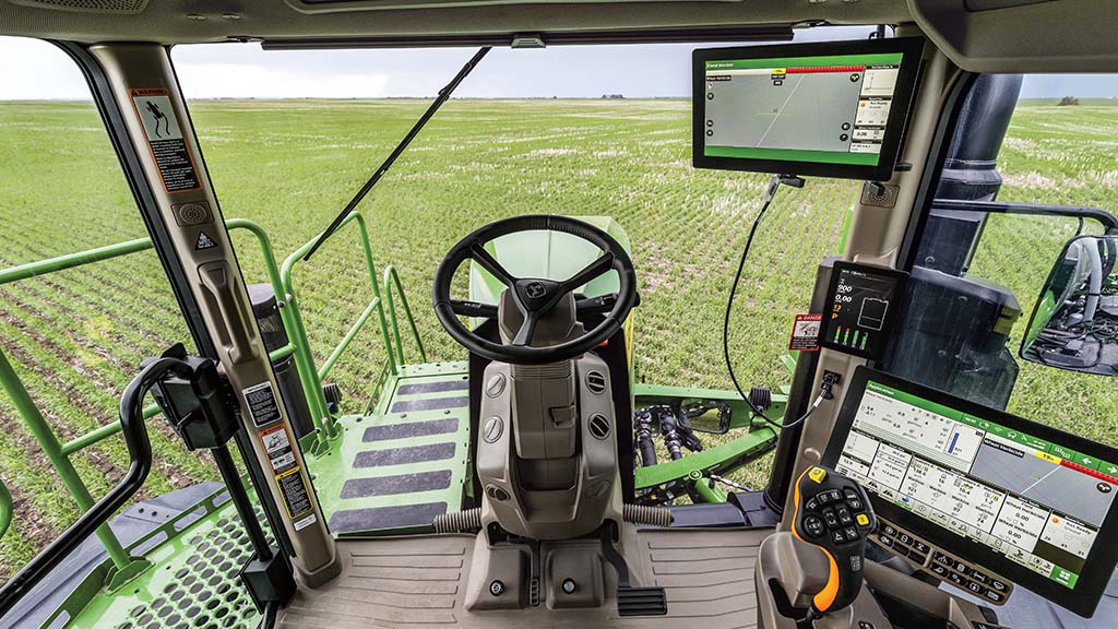 Vue depuis l’intérieur de la cabine d’un pulvérisateur automoteur John Deere surplombant un champ.