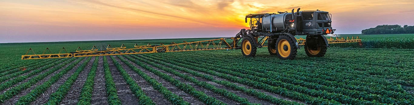 Hagie sprayer with front-mounted hybrid boom in field.