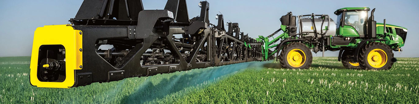 Photograph shot from the side showing a See&Spray-equiped John Deere Sprayer in a field with its boom fully extended.