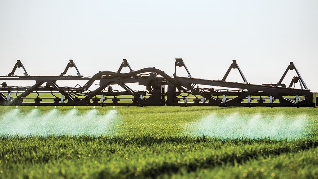 Close up view of sprayer boom with herbicide spraying on one side of the boom but not on the other side.