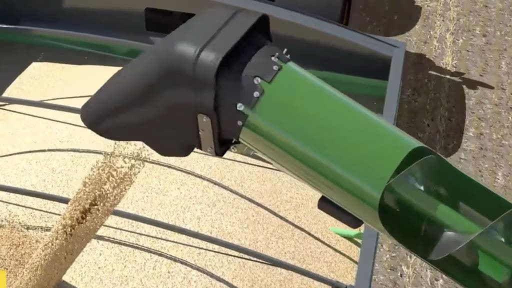 Gros plan de la machinerie agricole déchargeant le grain, présentant une goulotte verte distribuant les grains sur une surface sableuse.