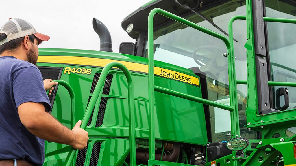 Un agriculteur monte sur un pulvérisateur 44038 de John Deere.