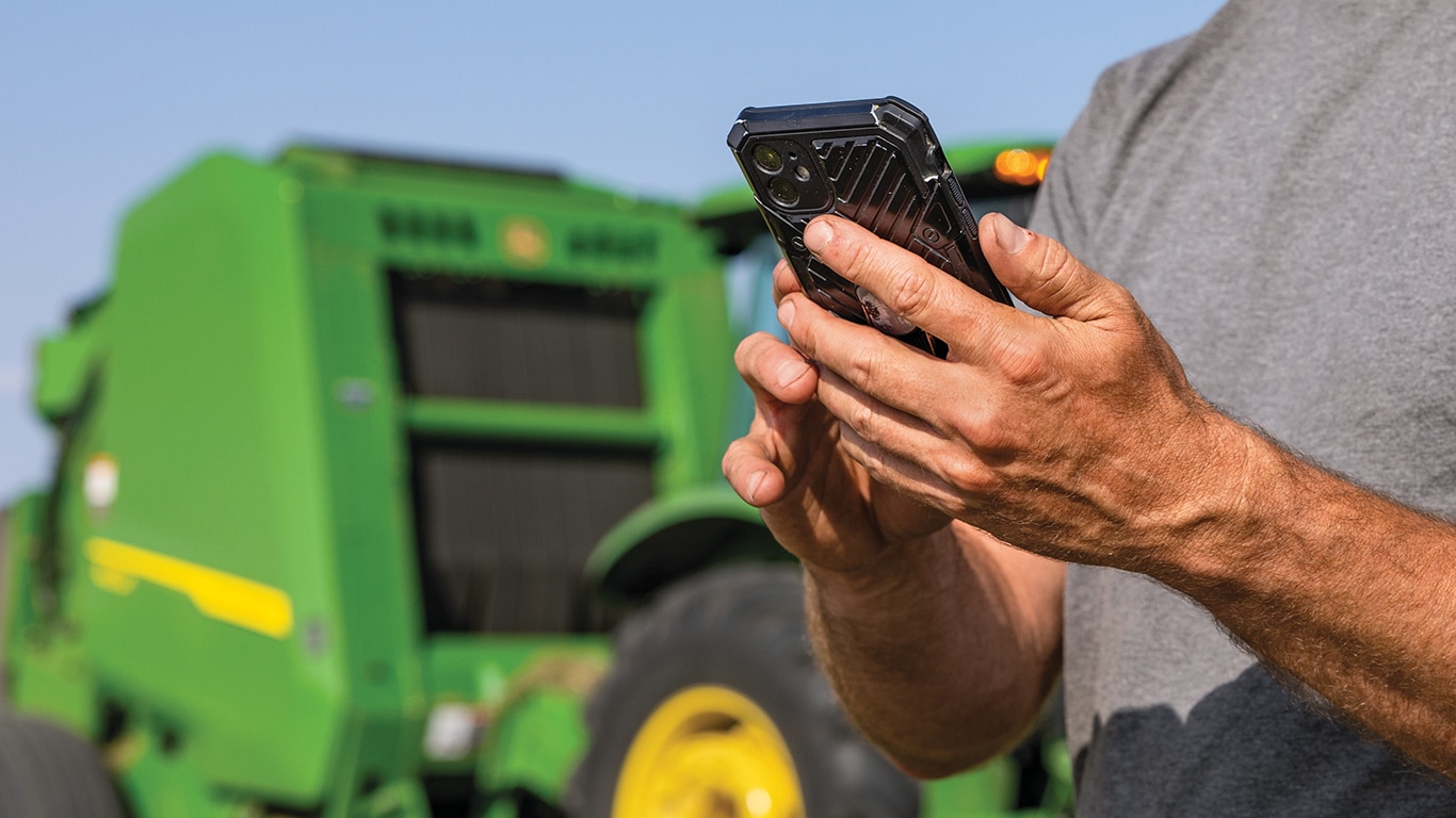 Farm worker using mobile device near green tractor in a field.