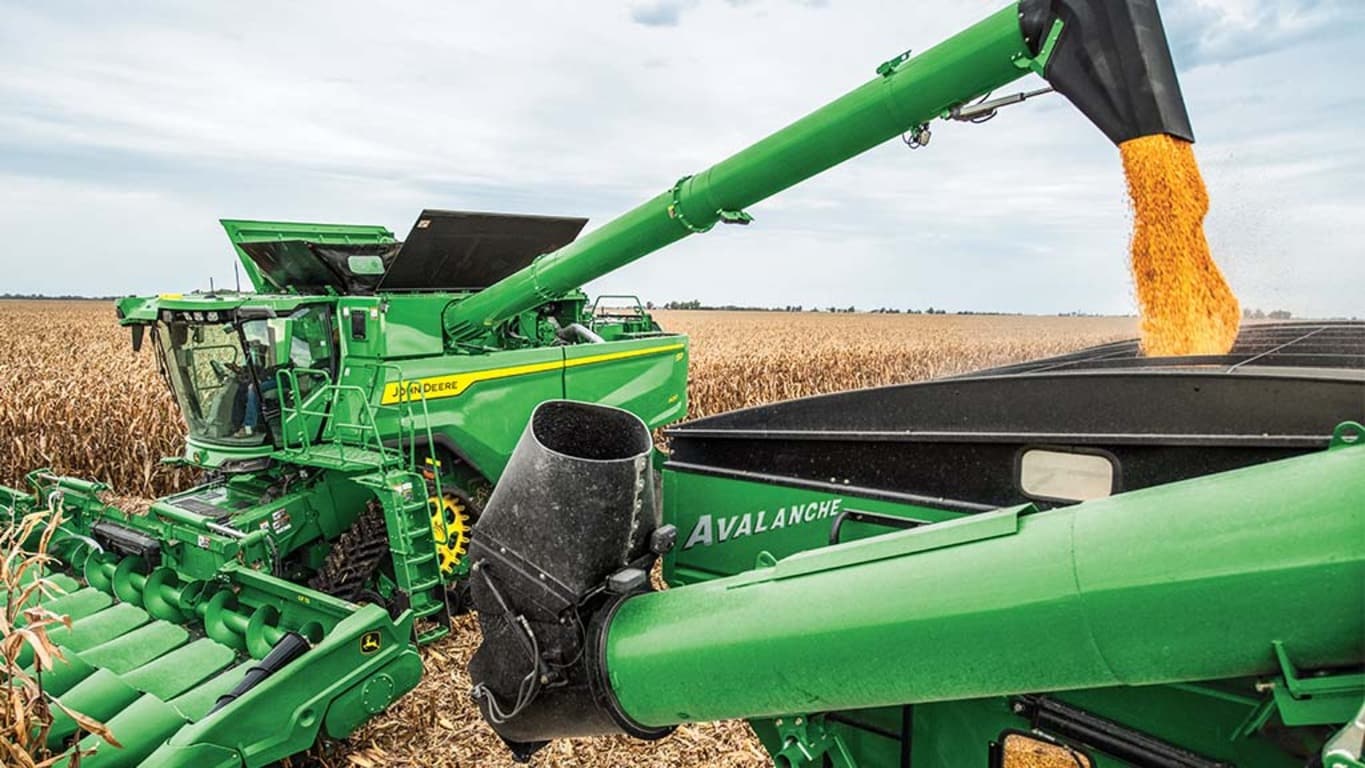 John Deere S7 Combine unloads corn on the go into a grain tank.