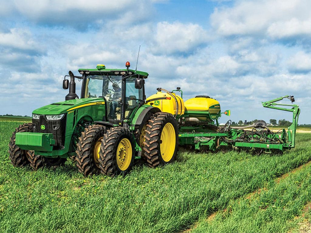Un tracteur vert avec des roues jaunes tire un outil jaune-vert à travers un champ.