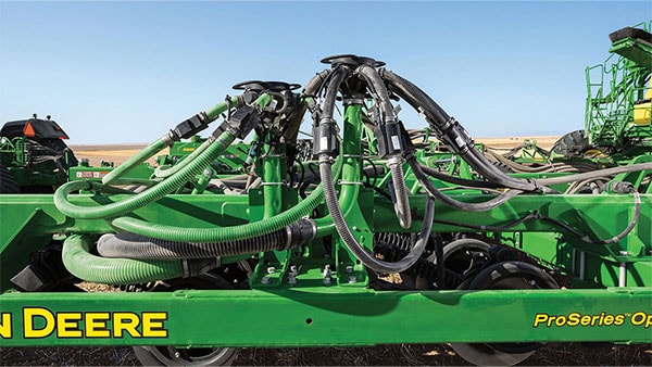 Close-up of a John Deere ProSeries planter toolbar showing seed distribution hoses and row unit components against a clear blue sky.