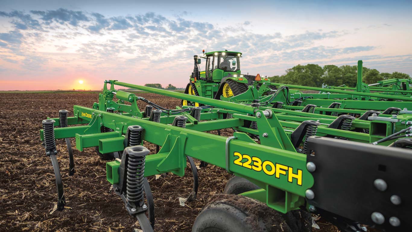 Un cultivateur prairie John Deere avec dents élastiques défonceuses mis en scène dans un champ au coucher du soleil.