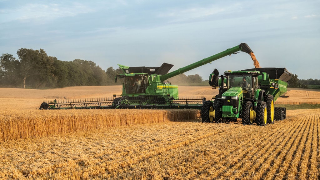 Une moissonneuse-batteuse verte déchargeant du grain dans une remorque placée à ses côtés pendant la récolte.