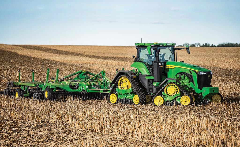 Tracked tractor pulling tillage equipment across a harvested field under clear sky.