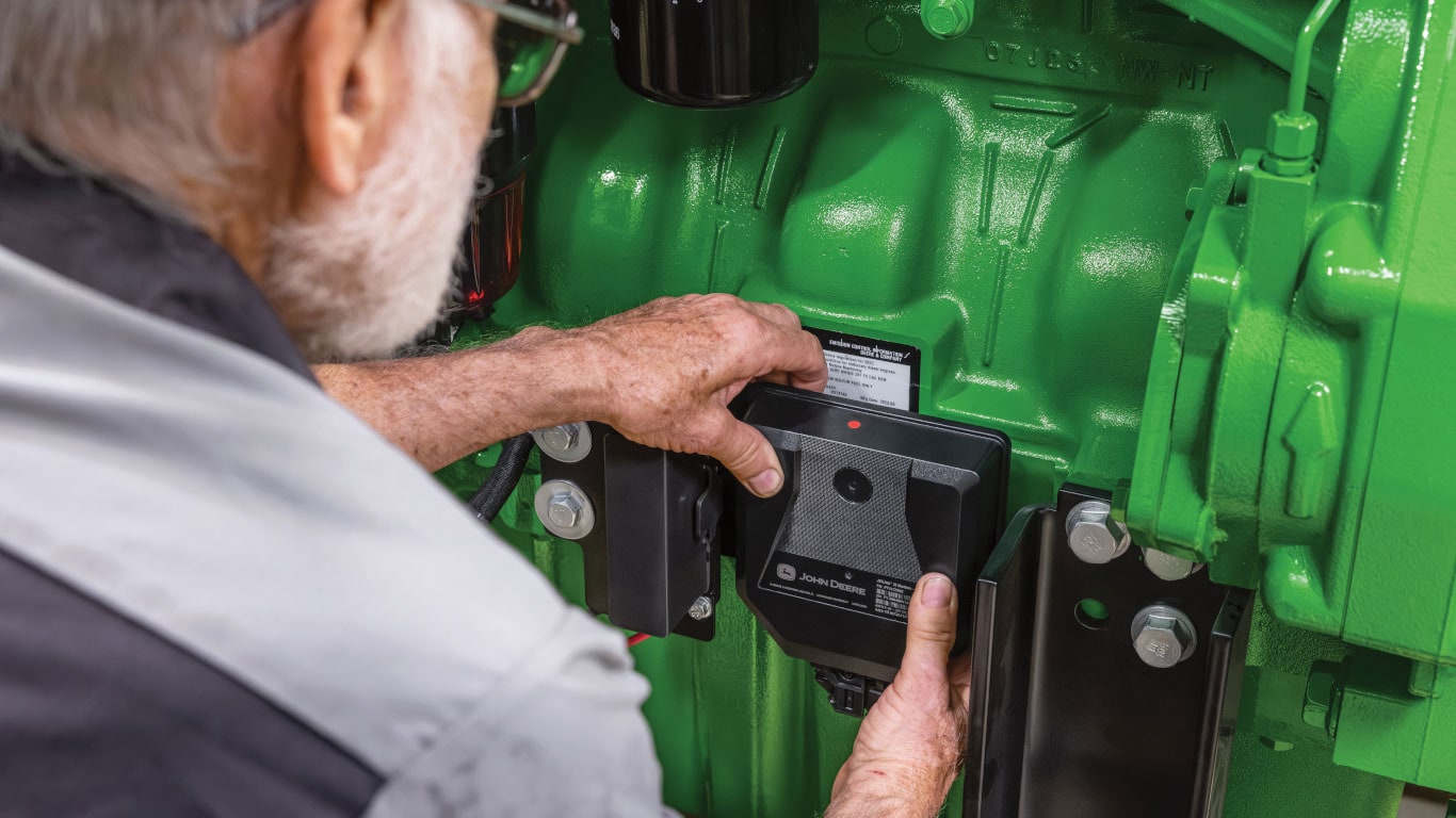Personne installant un modem John Deere JDLink noir sur un équipement vert.