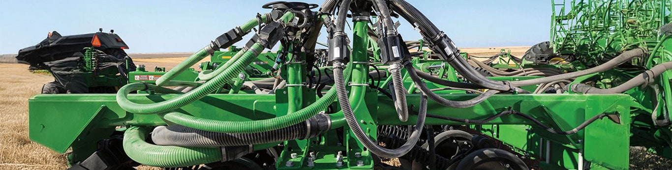 Close-up of a John Deere ProSeries planter toolbar showing seed distribution hoses and row unit components against a clear blue sky.