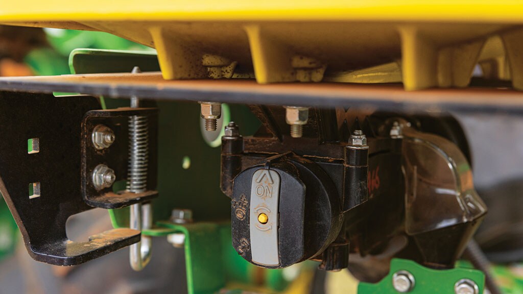 Close-up of an ON/OFF sensor with an amber indicator light mounted beneath a John Deere planter's yellow seed hopper.