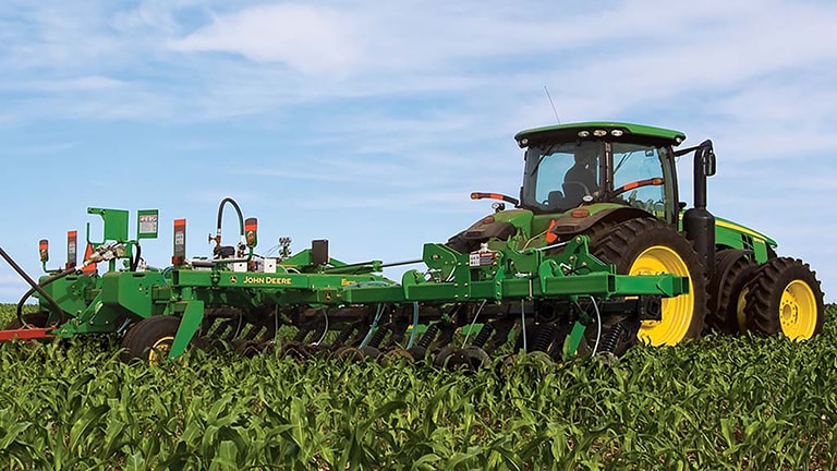 A green applicator tractor working in a corn field.