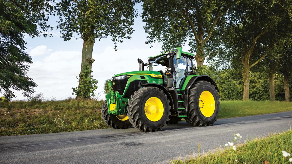 6R Tractor riding on a road next to a field.