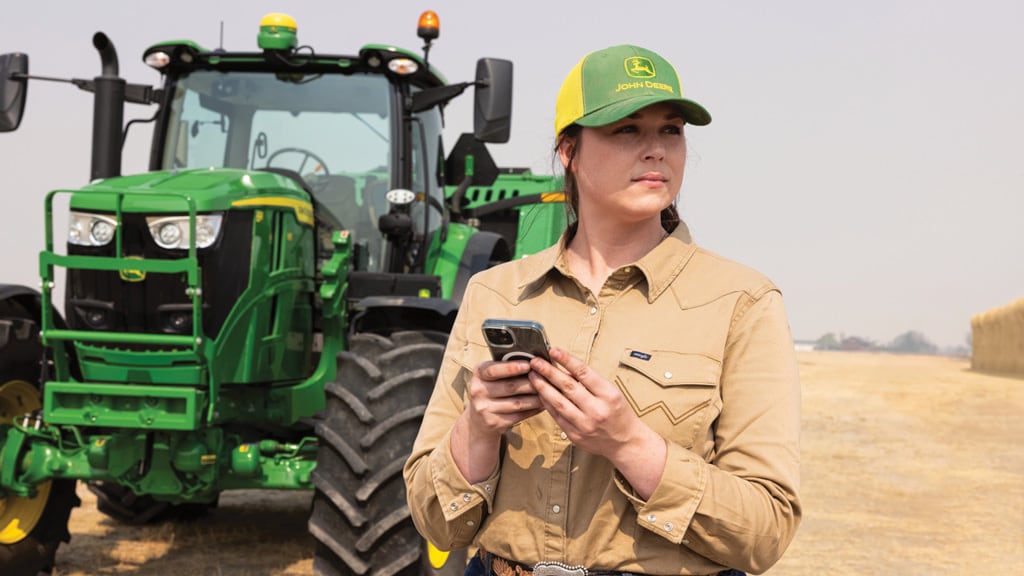 Farmer using a smartphone standing next to a 6 Series tractor.