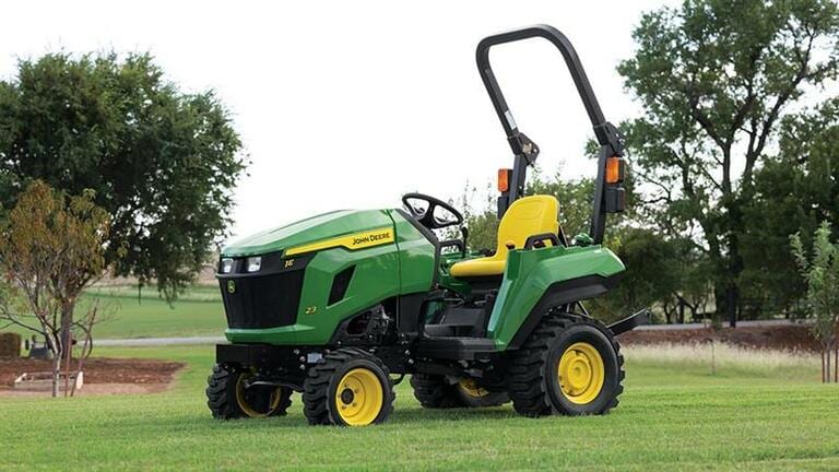 A flat open field has a green compact tractor with a yellow seat resting on it.