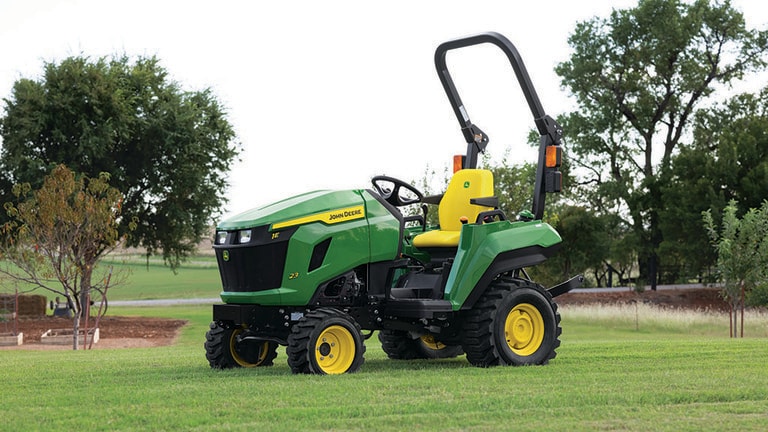 Dans un champ dégagé et plat, un tracteur compact vert avec un fauteuil jaune est à l’arrêt.
