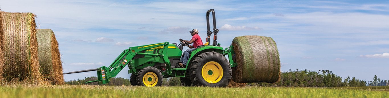 Person using a 4 series tractor equipped with bale spears to pick up round bale